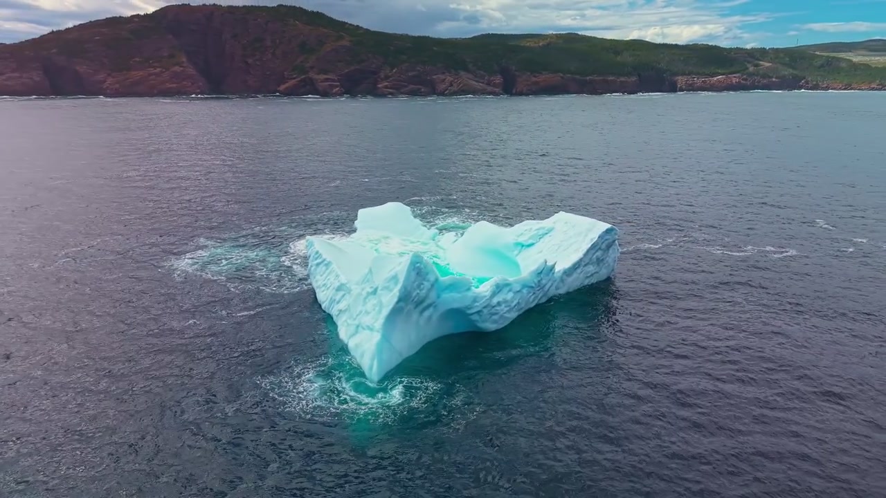 Aerial drone view of large flat iceberg with turquoise melt pool near St Johns coastline