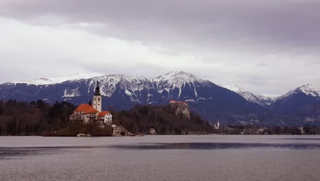 time lapse of an old catholic church on isolated island with mountain snow peak and bled lake. clouds moving faster through the day