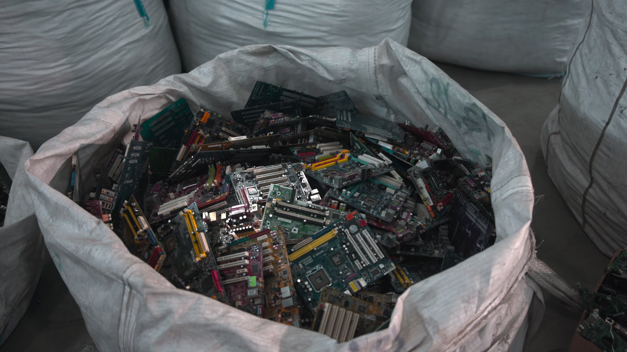 Large Sack Filled With Motherboards And Components, Dim Warehouse Setting, Overflowing White Bulk Bag Of Mixed . Media