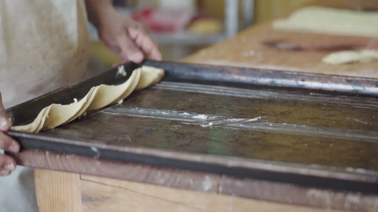 el pastelero arregla cuidadosamente las piezas de masa en una hoja de hornear, preparándose para hornear