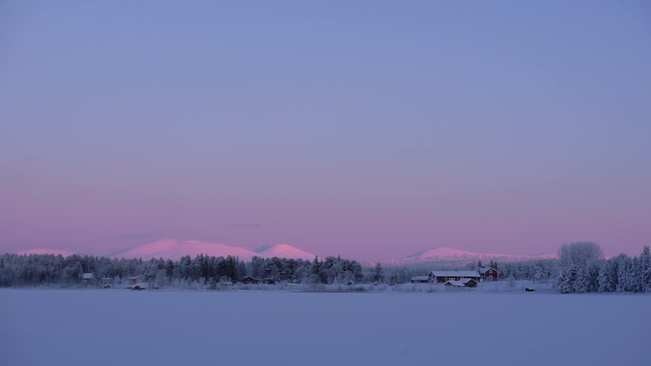 Panoramic landscape view of Lapland red buildings, near a snowcapped forest, at dusk, Finland