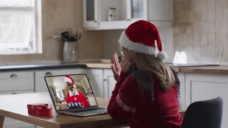 Caucasian-woman-wearing-santa-hat-on-laptop-video-chat-during-christmas-at-home