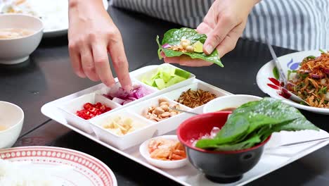 hands assembling traditional thai miang kham leaf wraps with ingredients