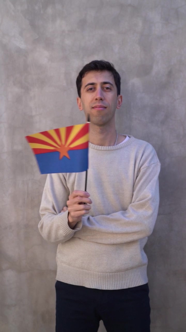Inquadratura verticale di un giovane adulto maschio che sventola la bandiera dello stato dell'Arizona. Al rallentatore.