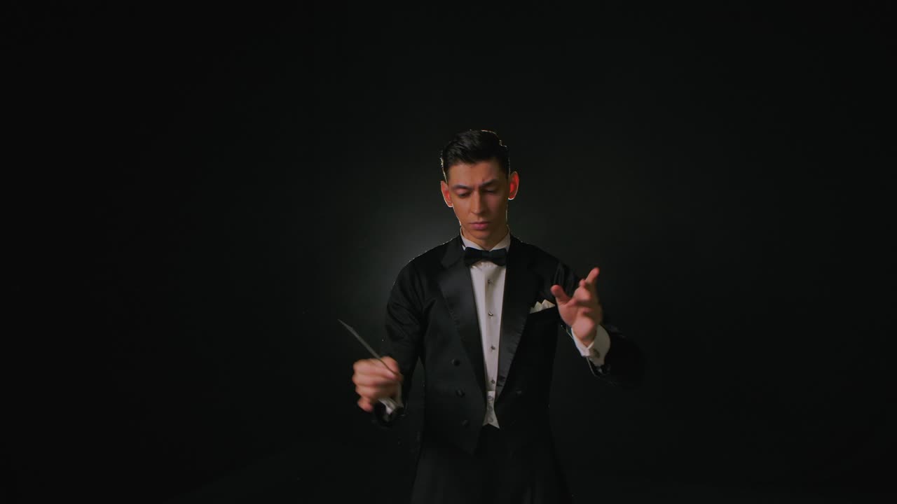 오케스트라 리더는 악보를 착용하여 음악가들을 동기화시키기 위해 지휘 지이를 사용한다. 마에스트로는 흑색 배경에서 연기와 백라이트와 함께 스틱의 움직임으로 음악가들을 지휘한다.