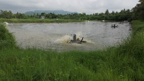 wide fixed view of tilapia fish pond with aeration devices in action. surrounded by vegetation and low hills