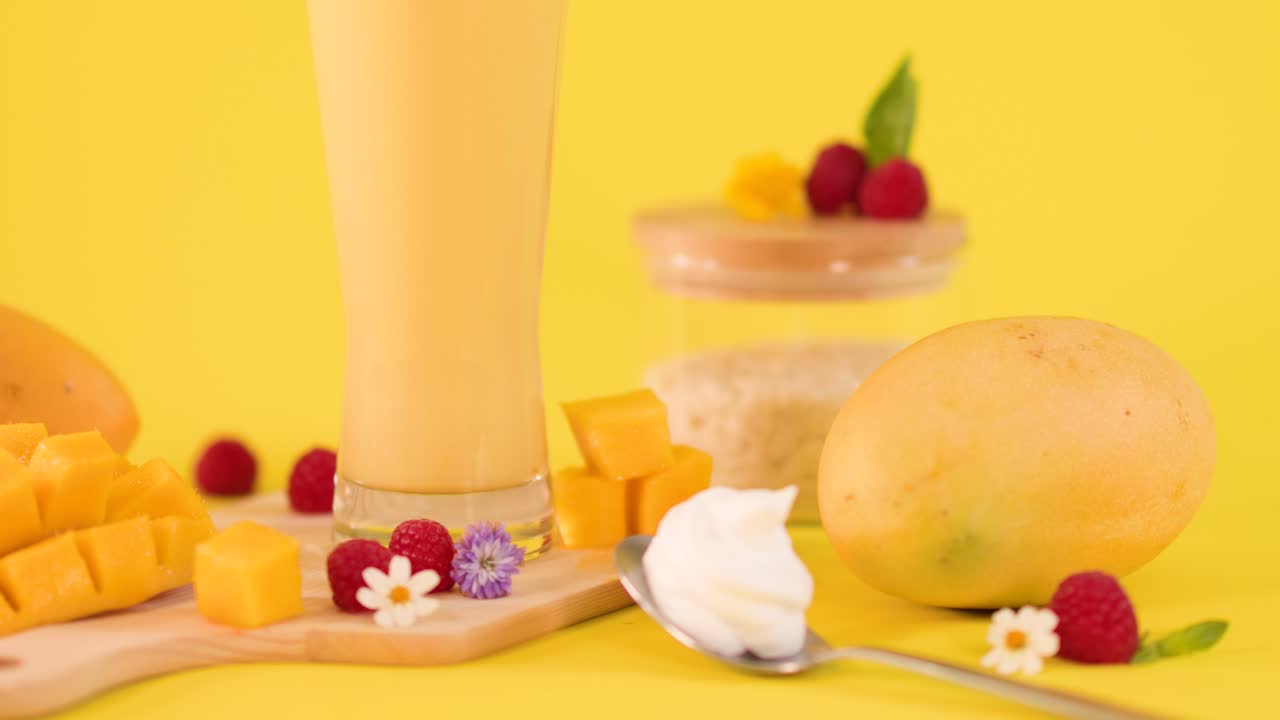 Primo piano rotante di un bicchiere di frullato al mango con frutta a fette, frutti di bosco, panna e sfondo luminoso
