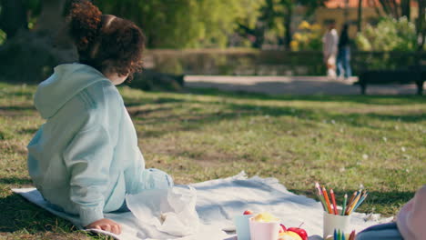 child sitting picnic in beautiful green grass meadow near unknown mother