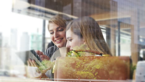 two woman friends sharing coffee using digital tablet in cafe