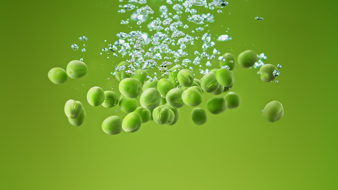Green Peas Dropped Into Water Making Bubbles And Sinking On Green Background, Slow Motion and Macro