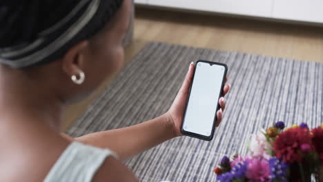 una joven afroamericana sostiene un teléfono inteligente en casa, con espacio para copiar