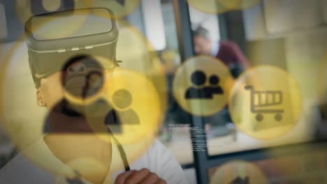 múltiples iconos digitales flotando contra un empresario afroamericano que usa auriculares vr en la oficina