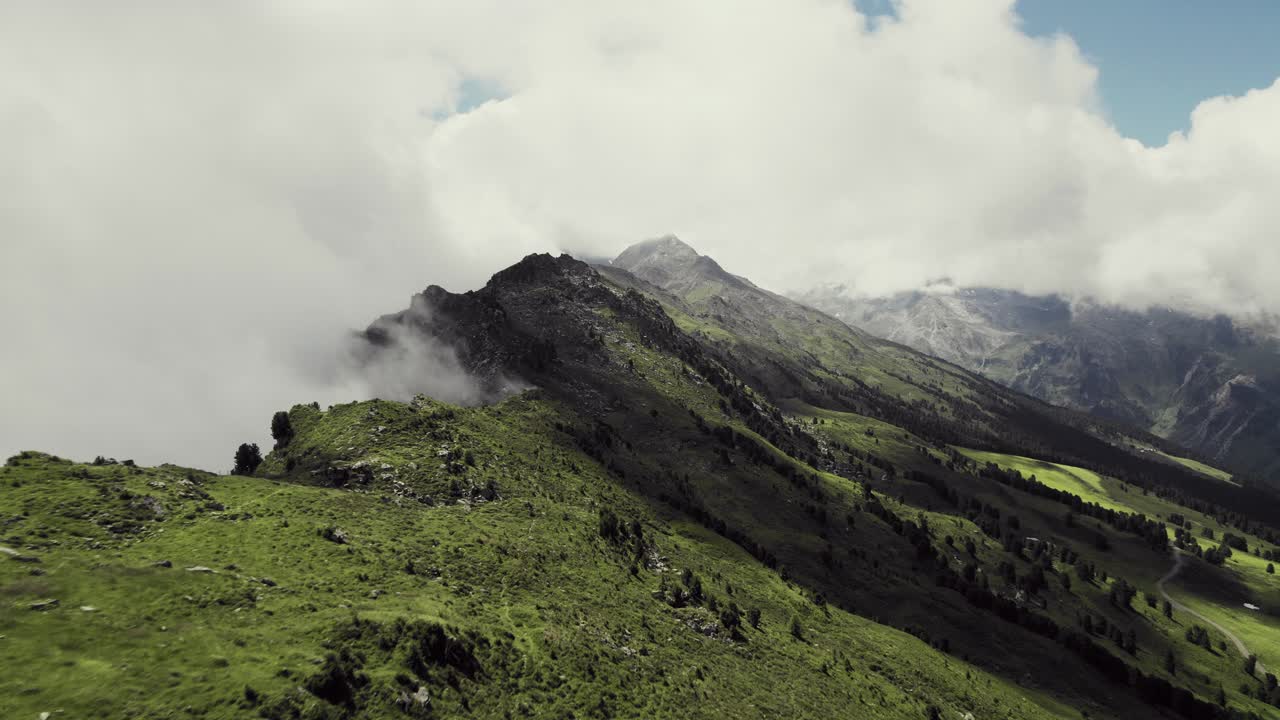 toma aérea de drones volando a lo largo de montañas cubiertas de hierba con un pequeño sendero que conduce a lo largo
