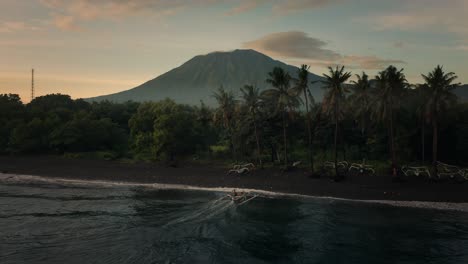 Traditionelles-Auslegerkanuboot,-Das-Am-Frühen-Morgen-An-Der-Tropischen-Küste-Ankommt,-Mount-Agung-Im-Hintergrund,-Antenne