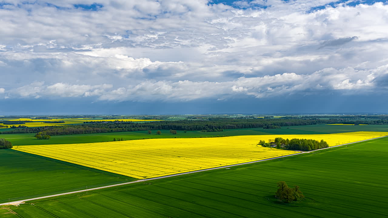 Clouds drift rapidly above vibrant green and yellow fields in a scenic time-lapse view.