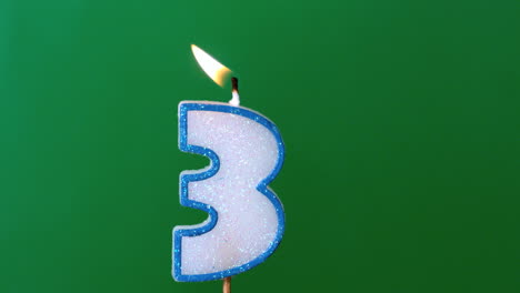 three birthday candle flickering and extinguishing on green background