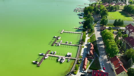 Aerial-view-of-a-marina-with-boats-docked-in-a-green-lake-in-Ryn,-Warmia-Masuria,-showcasing-a-picturesque-lakeside-town