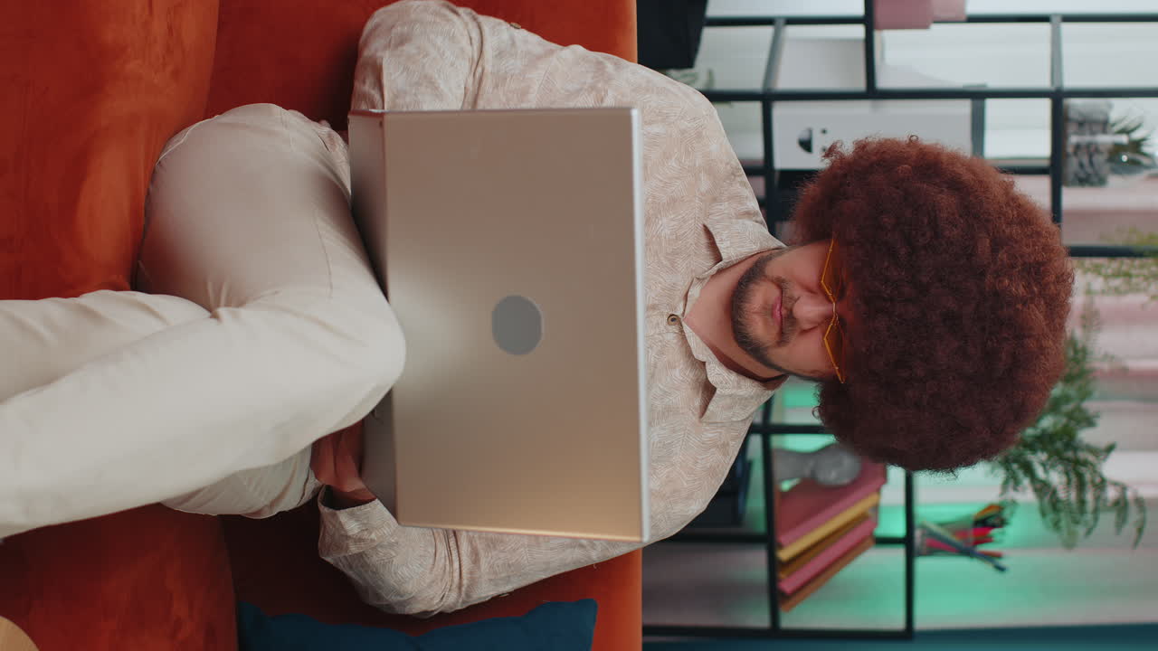 Young adult man freelancer starts working on laptop, sends messages, makes online purchases at home