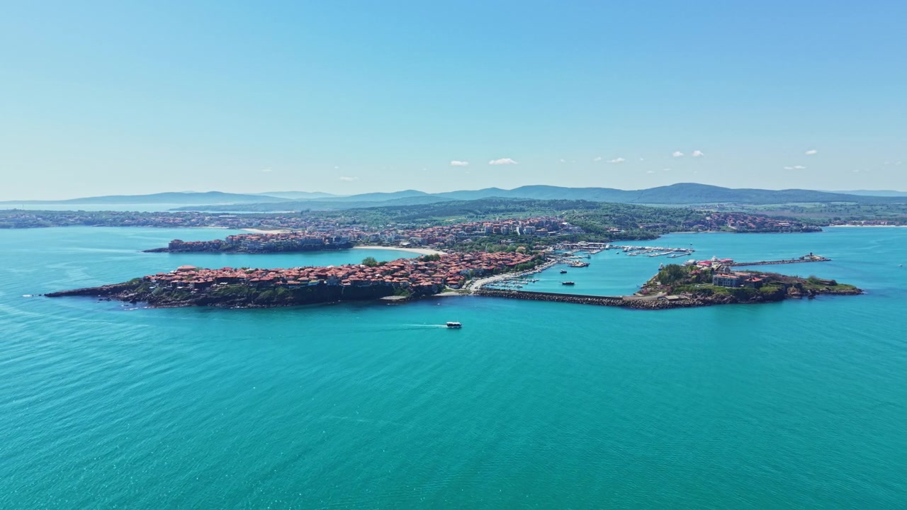 Güneşli bir günde su kenarında tekneler ve arka planda uzakta bir manzara ile bir sahil kasabası manzarası.