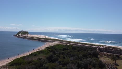 aerial view of a peninsula with a lighthouse and a beach where people walking