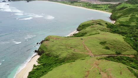 green meadow and white sand beach at bukit merese lombok surrounded by ocean, aerial