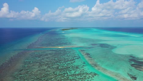 Peaceful-turquoise-lagoon-with-coral-reefs-barrier-around-atoll-and-tiny-tropical-islands-under-frozen-white-clouds-in-Maldives