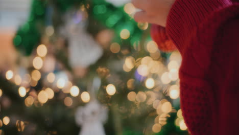 Female-hands-decorating-illuminated-Christmas-tree-with-bauble-at-home