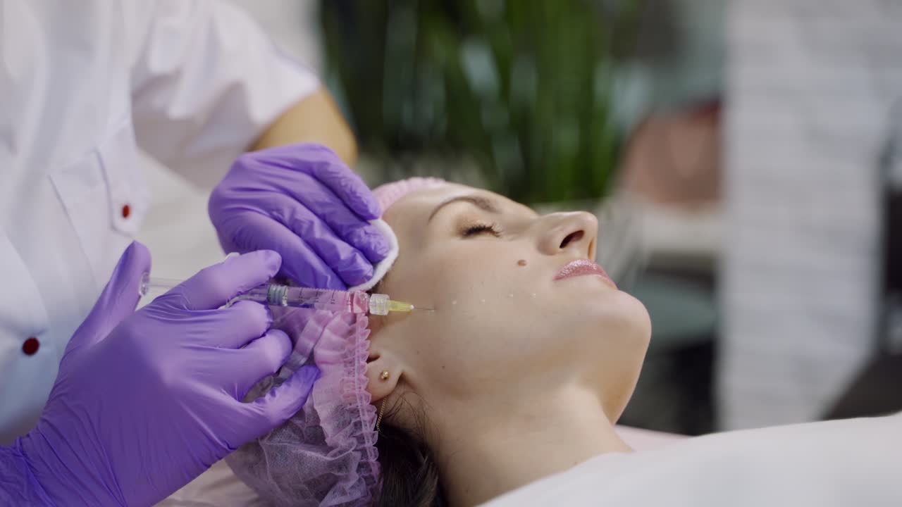 An experienced cosmetologist conducts mesotherapy for a woman who lays on a couch in the cosmetology office. Close-up