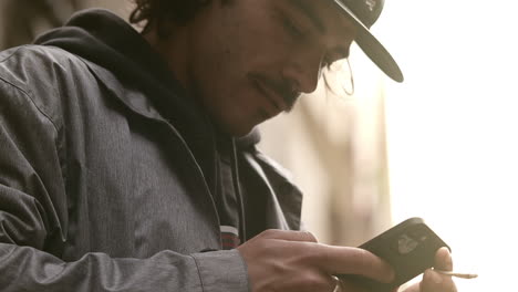 man with cap, cigarette in hand, looks at his mobile phone, social media, low angle