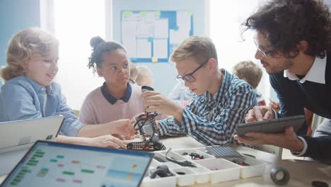 Elementary School Robotics Classroom: Diverse Group of Brilliant Children with Enthusiastic Teacher Building and Programming Robot. Kids Learning Software Design and Creative Robotics Engineering