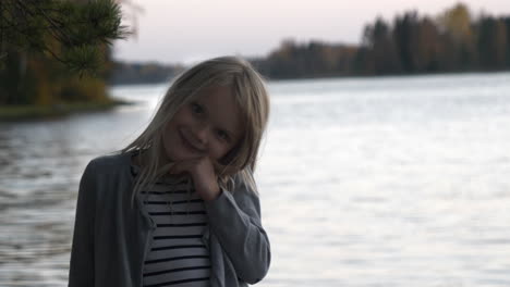 young female child with blonde hair turning towards camera and smile with lake water in background