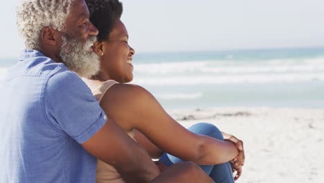 Glückliches-Afroamerikanisches-Paar,-Das-Am-Sonnigen-Strand-Sitzt-Und-Sich-Umarmt