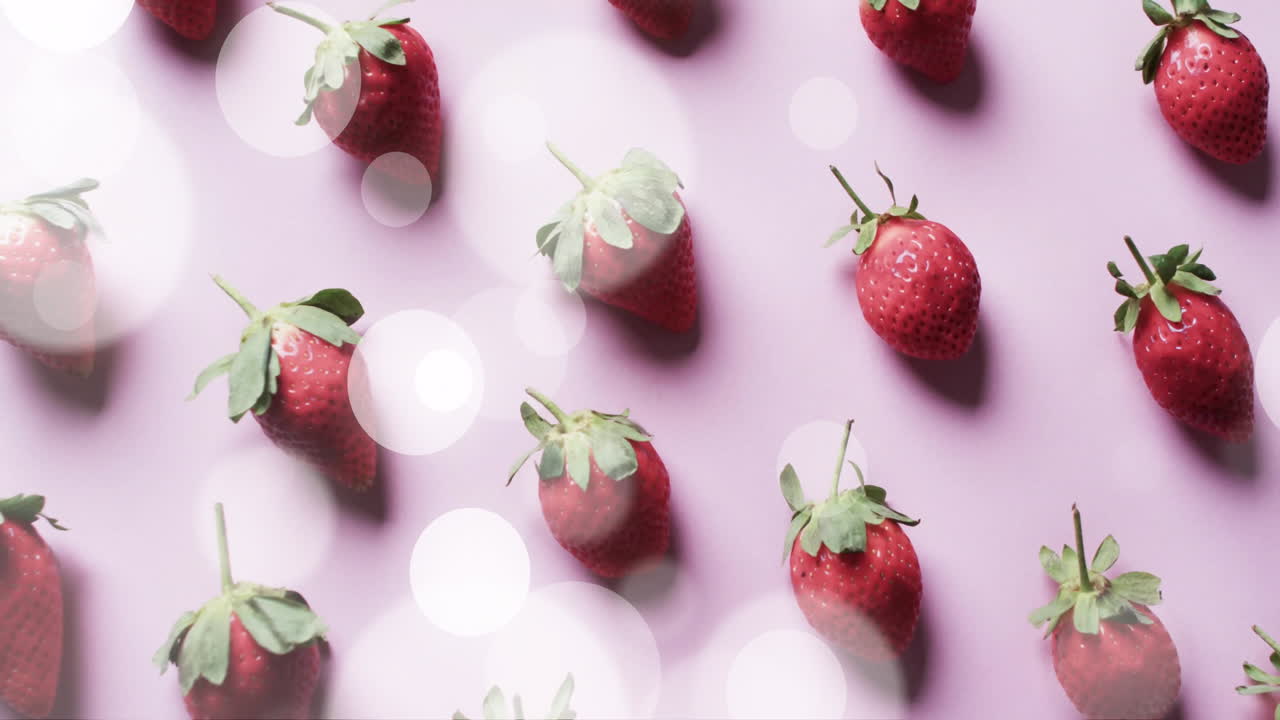 Composition of spots of light over strawberries on pink background