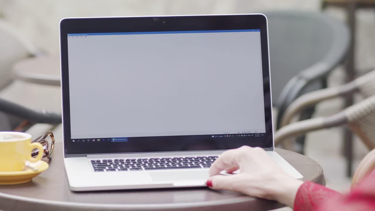 Over-the-shoulder shot of a woman's hand using the track pad on a laptop at a cafe. The screen is blank, providing a perfect mock up for your website, app, or video content.