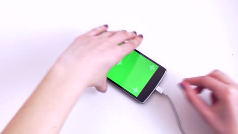 manos de mujer conectando el cable al teléfono inteligente con pantalla clave de croma verde sobre fondo blanco
