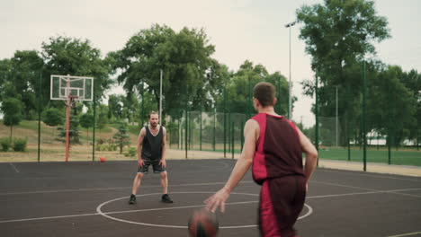 un hábil jugador de baloncesto regateando el balón entre las piernas contra su defensor contrario y lanzando el balón al aro de baloncesto al aire libre