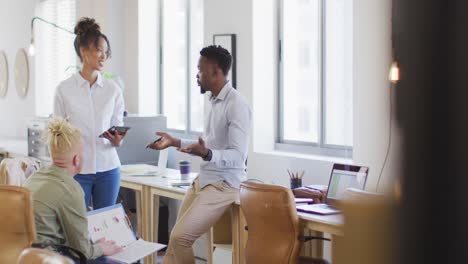 Happy-diverse-business-people-discussing-with-tablet-in-creative-office