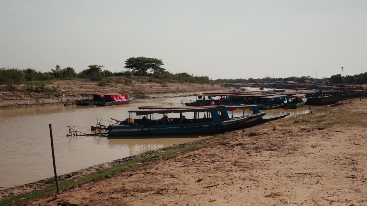 Barche turistiche ormeggiate lungo una riva fangosa e poco profonda vicino al lago Tonle Sap in Cambogia