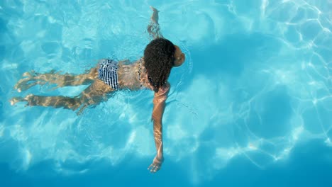 High-angle-view-of-young-mixed-race-woman-swimming-in-pool-on-a-sunny-day-4k