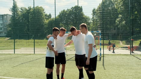 Fröhliche-Junge-Straßenfußballspieler-Mit-Ball,-Die-Im-Kreis-Stehen-Und-Sich-Vor-Fußballspiel-1-Auf-Dem-Spielfeld-Umarmen