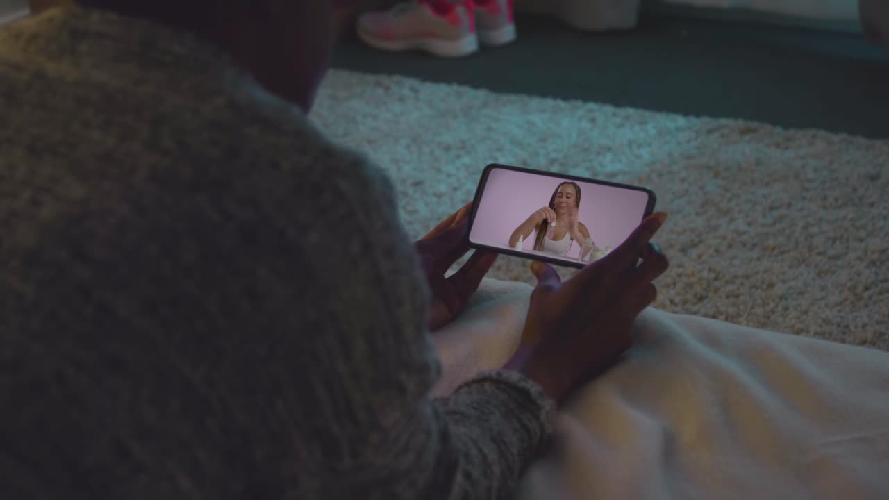 mujer acostada en la cama en casa mirando el video de demostración de productos de belleza en el teléfono móvil