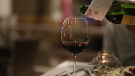 a sequence showing red wine being poured into a glass at a sophisticated dining setting with warm lighting