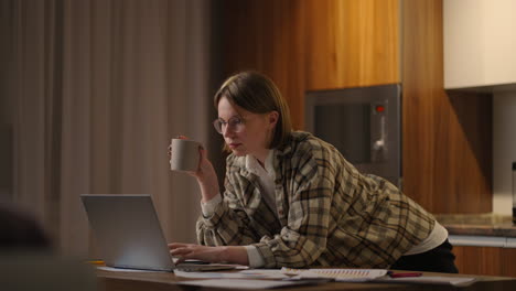 beautiful young woman working on laptop computer while sitting at the living room drinking coffee. happy casual beautiful woman working on a laptop. working at home with laptop and documents