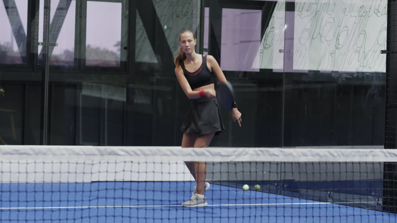 Woman playing padel tennis on indoor court, focusing on hitting ball
