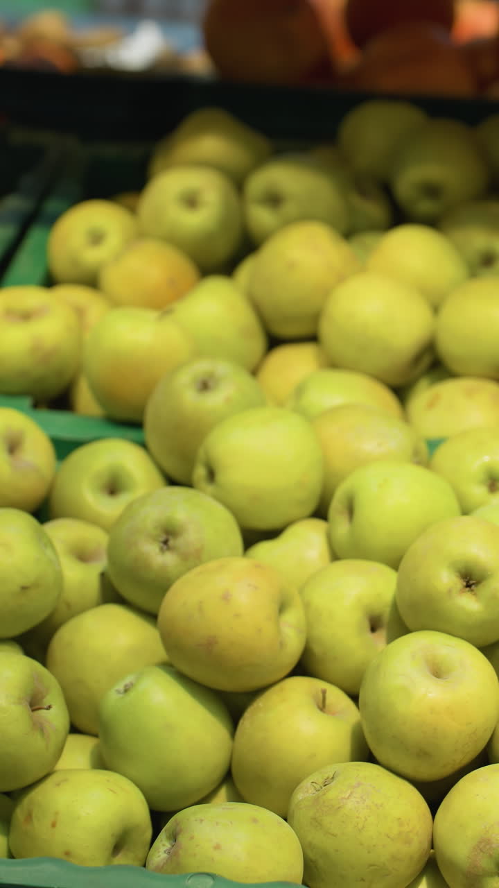 검은 코트와 구슬 팔를 입은 손이 식료품 가게의 상자에서 두 개의 사과를 집어 들고 있는 모습.