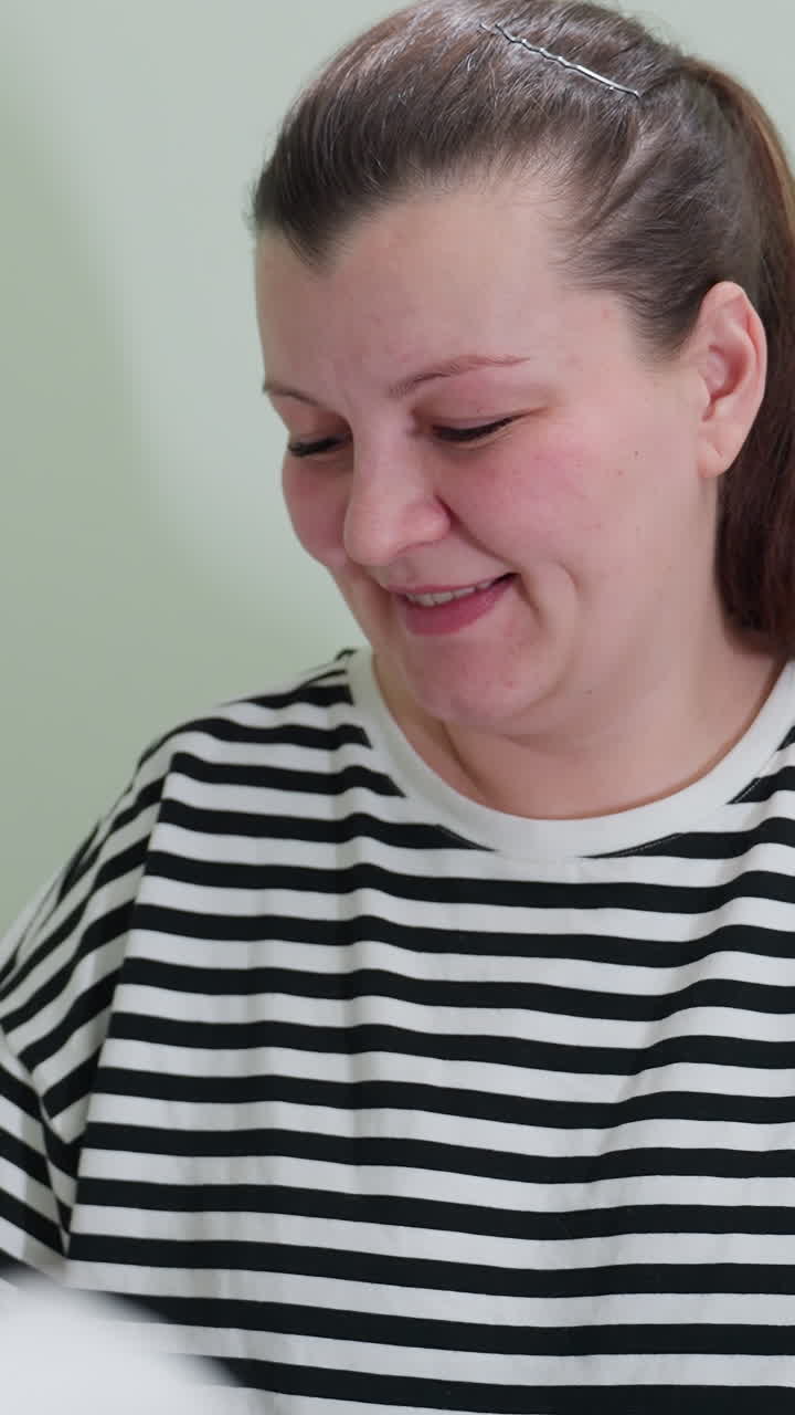 Mujer relajada examinando un documento con una sonrisa cálida, mujer informal mirando un papel en el interior con expresión amable, mujer caucásica alegre con ropa de rayas revisando un documento en el interior con tranquilidad