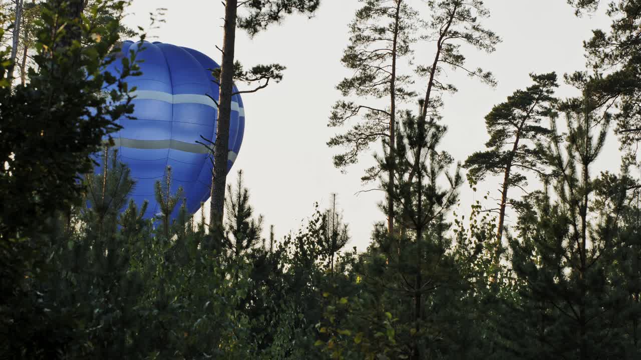 A vibrant hot air balloon floats among trees during sunset.