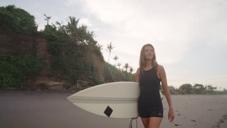 schöne frau, die mit ihrem surfbrett an einem sandstrand spazieren geht, während sie den ozean beobachtet