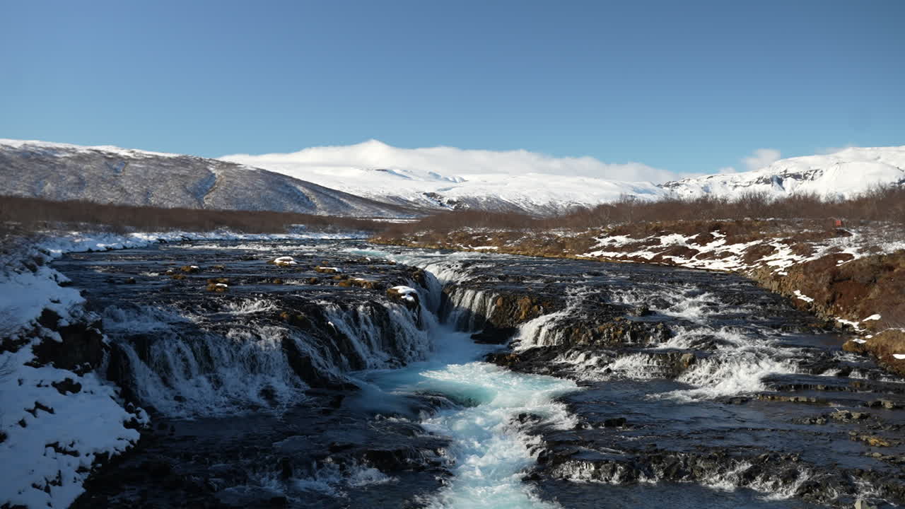Brúarfoss flows through snowy lava fields beneath Icelandic mountains. Laugarvatn, Haukadalur, Iceland