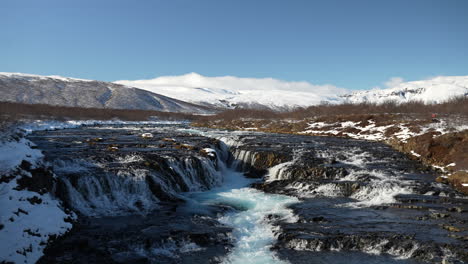 brúarfoss flows through snowy lava fields beneath icelandic mountains. laugarvatn, haukadalur, iceland
